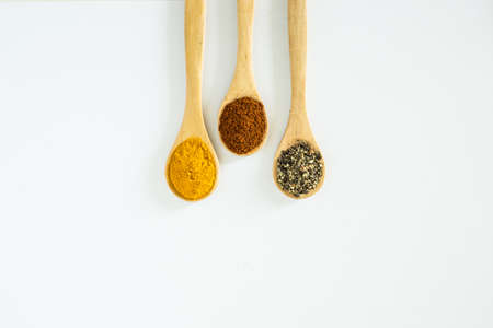 Turmeric, Paprika and Black Pepper ground in wooden spoon over white background.の写真素材