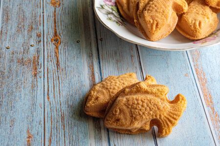 Traditional Malaysian cake called "kuih bahulu or baulu" in fish shape, in flowery plate over wooden background.の写真素材
