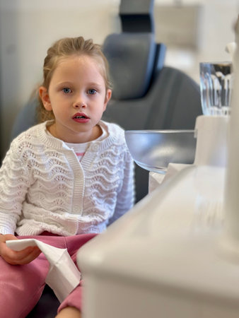 Adorable little girl sitting at dental chair in clinic and looking at cameraの写真素材