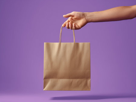 Female hand holding brown paper shopping bag on purple background. Mock upの素材