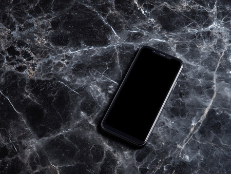 Smartphone with blank screen on black marble background. Top view.の素材