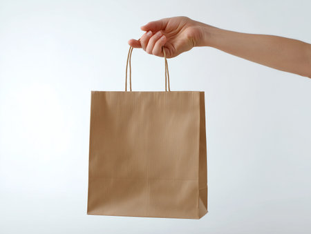 Female hand holding brown paper shopping bag isolated on white background, clipping path includedの素材