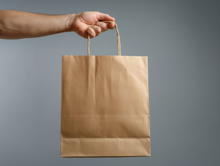 Brown paper bag in hand isolated on gray background. Close up.の素材