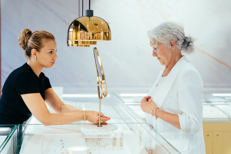 Happy senior woman choosing and buying some jewelry in modern boutique. Blond woman owner, saleswoman of jewelry shop presenting ring.の写真素材