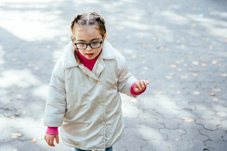 Focused child curious girl with two braids in eyeglasses, white coat smiling enjoying good sunny weather in autumn park outdoor.の写真素材