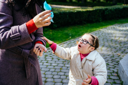 Sad crying little girl with two braids in eyeglasses looking up at unrecognizable mother at autumn...