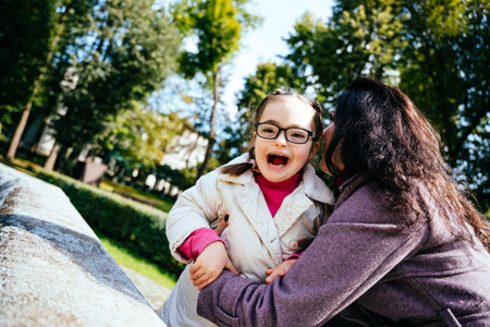 Lovely child in eyeglasses with cute facial expression with her mother outdoor. Child feeling love from parent.の写真素材