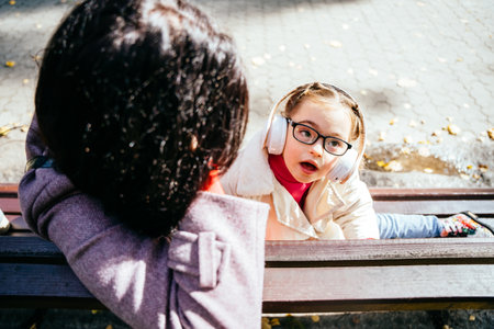 Cute lovely child girl with disability listening music with dreaming expression on face and mother in park outdoor.の写真素材