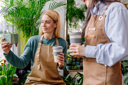 Store owner middle age blond female working taking care of the plants in pot her assistant helping doing inventory at cozy plant store.の写真素材