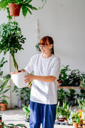 Florist red haired woman in glasses holding a plant at pot. Home gardening, love of plants and care. Small business.の写真素材