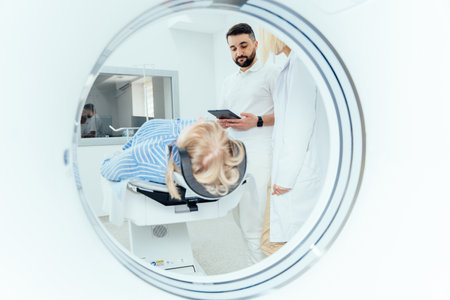 Radiographer operating computed tomography scanner being used to scan lying patient in radiology department of hospital. Doctor holding a tablet and looking at the patient.の写真素材