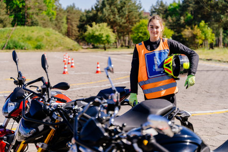 Happy beautiful woman wearing a safety vest and helmet stands next to a motorcycle. Learning to ride...