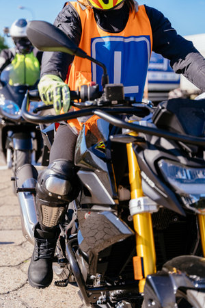A man in a black jacket and orange vest is riding a motorcycle. He is wearing a helmet and gloves....
