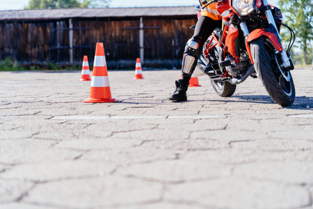 L-driver female driver with helmet taking motorcycle lessons and practicing ride. slalom through the orange cones on motordrome on motorcycle. Motorcycle school of driving.の写真素材
