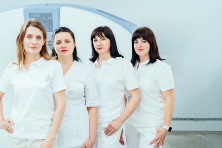 Four women in white shirts stand in row in front of a machine. They are all wearing white uniforms...