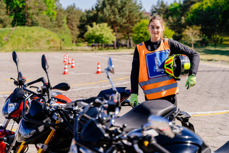 A woman L-driver wearing a safety vest and helmet stands next to a motorcycle. Female smiling and...