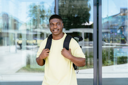 Travel, adventure, booking, destination, concept. Happy black guy traveler in sunglasses with backpack walking down the street in urban modern city, smiling and looking away. African man spending time outdoors.の写真素材