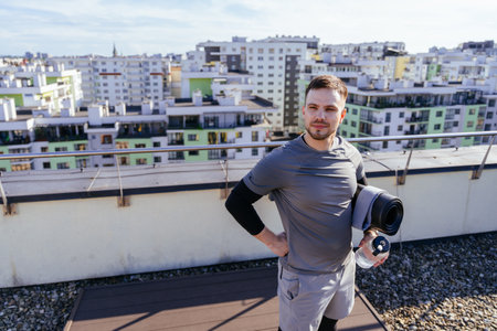 Bearded sporty handsome man going to workout Gym or yoga practice on rooftop with a mat and a bottle of water in hands. walk outdoors outside.の写真素材