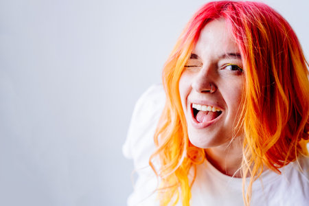 Young Caucasian woman with vibrant red and orange hair winks playfully at camera, exuding energy and positivity, fun and individuality. Youthful spirit and creativity. Close-up shot.の写真素材