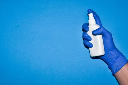 Hand in a medical glove holds an antiseptic for the treatment of hands on a blue background. Safety. The concept of viruses.の写真素材