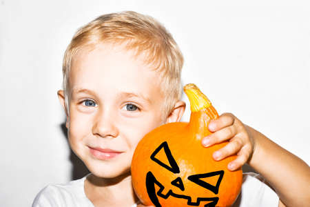 Halloween holiday concept. Cute little kid with pumpkin on a white background. Happy little boy holding a Halloween pumpkin.の写真素材