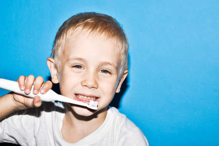 Happy child kid boy brushing teeth with electric toothbrush on blue background. Health care, dental hygiene. Mockup, copy space.の写真素材