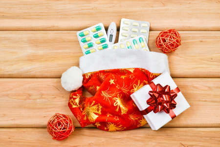 Medical Christmas. Pills, gift present box, Santa Claus hat, thermometer on a wooden background. Medical concept. Greeting card. New Year and Christmas. Copy space, flat lay.の写真素材
