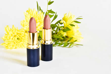 Decorative cosmetics. Pink lipstick and yellow chrysanthemum flowers on a white background. Place for text. Beauty conceptの写真素材