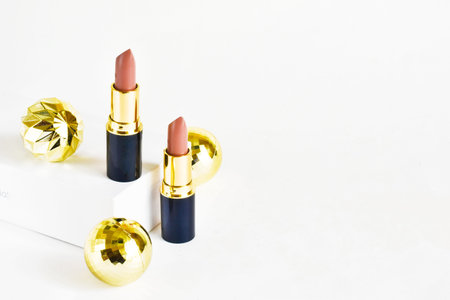 Light brown lipsticks on a white background with Christmas golden balls. Christmas gift for women....