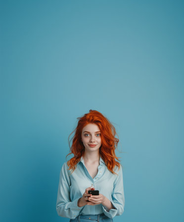young redhead woman with long hair using smartphone isolated on blue backgroundの素材