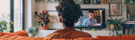 back view of african american man watching movie on tv at homeの素材
