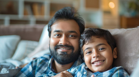 indian father and son looking at camera on sofa in living roomの素材