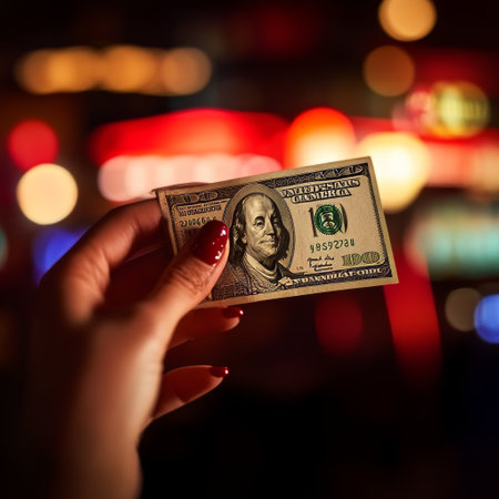 Female hand holding a dollar banknote against the background of the night cityの素材