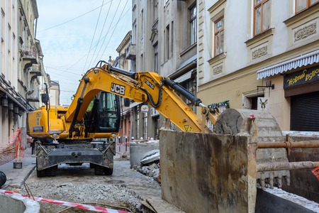 Ukraine, Lviv - December, 17, 2016: Repair of the aqueduct in the city center of Lviv on the narrow street. Construction machinery. Excavation work at the construction site.のeditorial素材