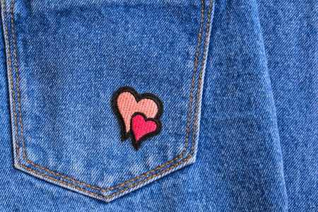 Fragment of jeans trousers with a pocket decorated with pink and red hearts. Denim background.の写真素材