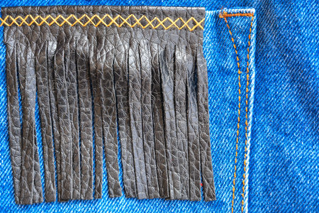 Fragment of jeans trousers with a pocket decorated with leather fringes and decorative stitching....
