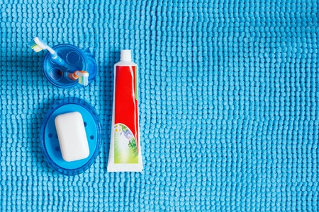 Blue glass with toothbrushes, tube of toothpaste and soap dish with white soap.の写真素材