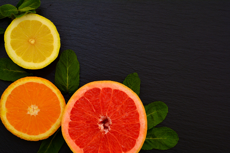 Half of juicy ripe grapfruit, orange and lemon with mint leaves on black slate board, plate, tray. Citrus fruit fresh.の写真素材