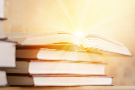 Pile of books with open book with rays of light. The concept of knowledge and enlightenment. Bookshelf with piled books.の写真素材