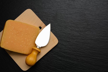 Slice of hard cheese and knife on board, plate or tray of black slate. Dark textured background.の写真素材