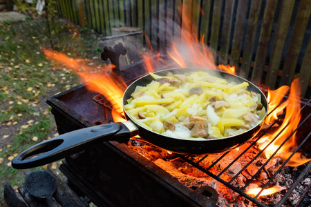 Frying pan with fried potatoes and mushrooms over an open fire. Cooking food on a fire in the yard.の写真素材