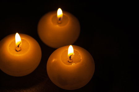 Burning bright golden candles on black background. Festive or morning candles.の写真素材