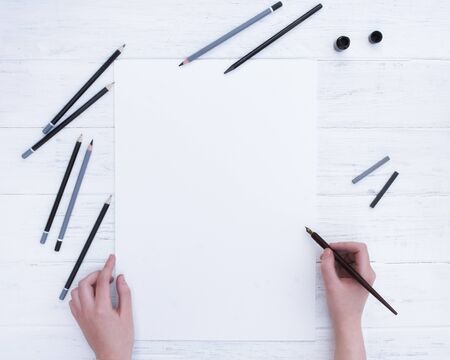 Mock up for calligraphy.  Hands holding the empty white paper sheet, and a calligraphy pen. A few pencils and black compressed charcoalの写真素材