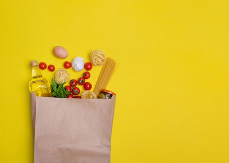 Olive oil, pasta, tagliatelle, olives, egg, cherry tomatoes, garlic in a paper bag on yellow backgroundの写真素材