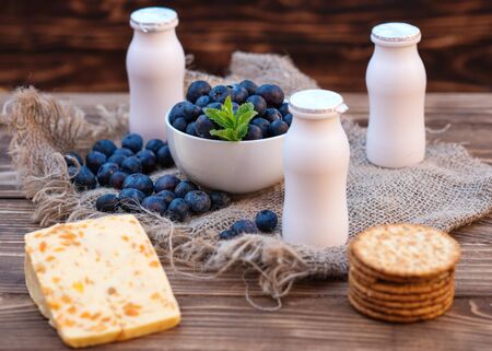 Fresh summer blueberry with leaf in the white bowl, yogurts bottles on the brown wooden backgroundの写真素材
