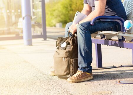 Green travel backpack, hat, maps, glasses on the platform at the  train station during quarantine and  man in the background at the sunsetの写真素材