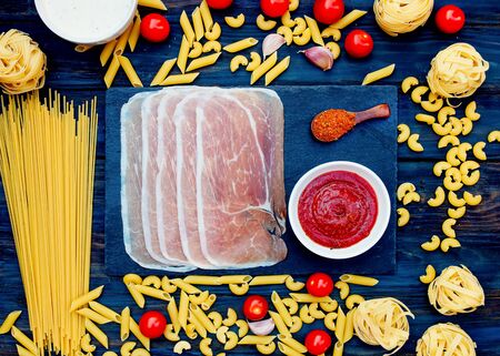 Spaghetti, tagliatelle, pasta, tomatoes, cherries, ham, sauce on wooden backgroundの写真素材