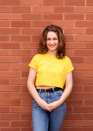 portrait of a young woman wearing yellow shirt against brick wallの写真素材