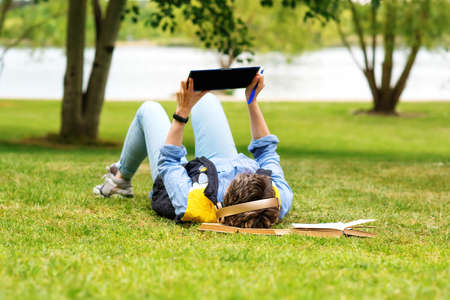 Woman lying on green grass and studying online on tabletの写真素材