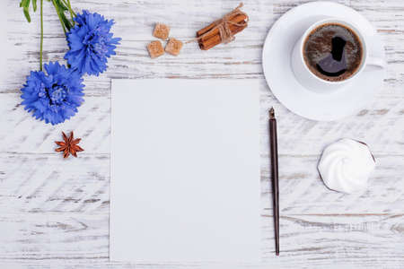 Mock up of empty paper, white cup of coffee, flower, ink pen, cake, shuga, anise and sinnamon on white wood desk. Flat Lay with no people. View from the top.の写真素材